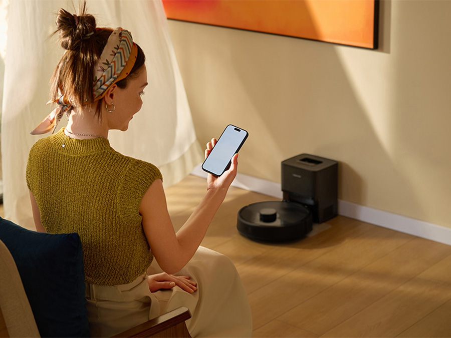 Frau sitzt in hellem Wohnzimmer und steuert den Saugroboter Roborock Q7 TF Schwarz über die mobile App