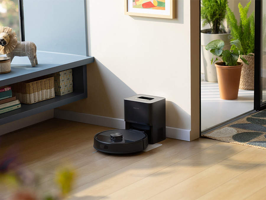 Saugroboter Roborock Q7 TF Schwarz kehrt zur Dockingstation zurück, die an einer Wand in einem hellen, gemütlichen Raum steht
