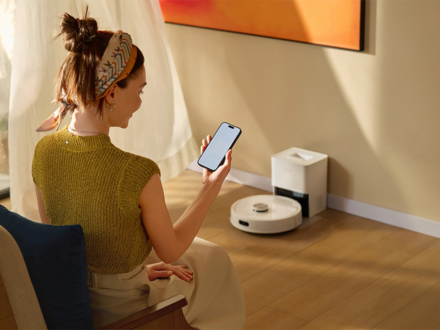 Frau sitzt in einem hellen Wohnzimmer und steuert den Saugroboter Roborock Q7 TF Weiß per mobiler App