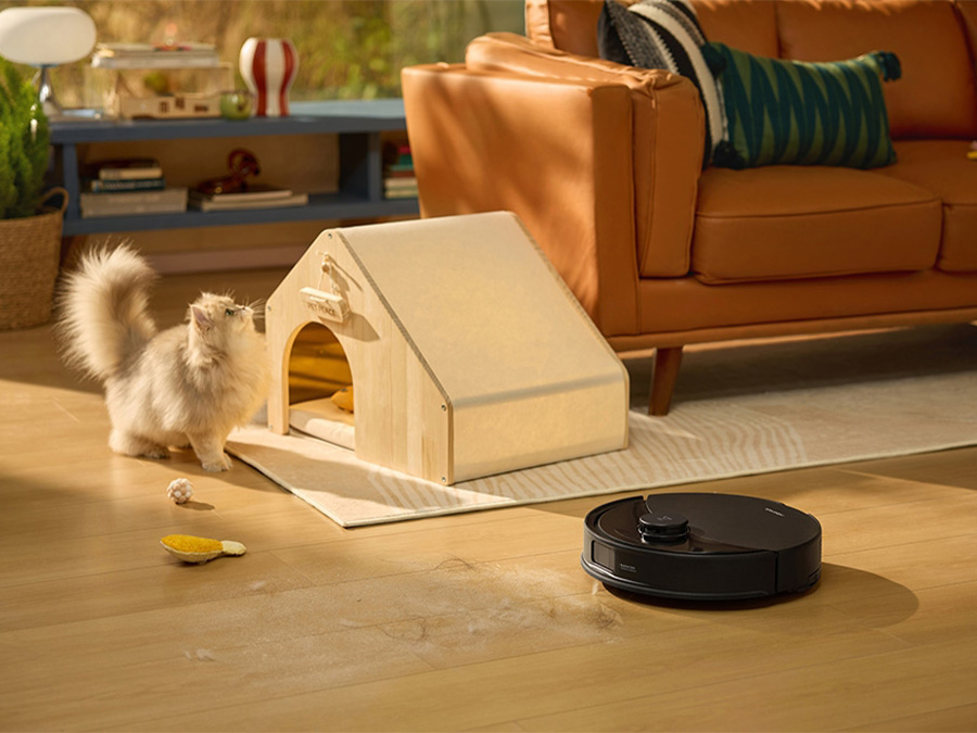 Saugroboter Roborock Q10 bei der Arbeit im Wohnzimmer; Katze spielt neben dem Körbchen, Haare und Spielzeuge auf dem Boden