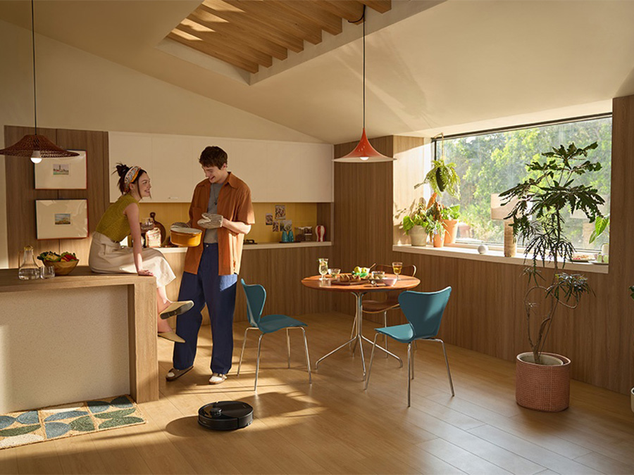 Saugroboter Roborock Q10 PF Black reinigt die Küche; im Hintergrund ein Paar beim Kochen