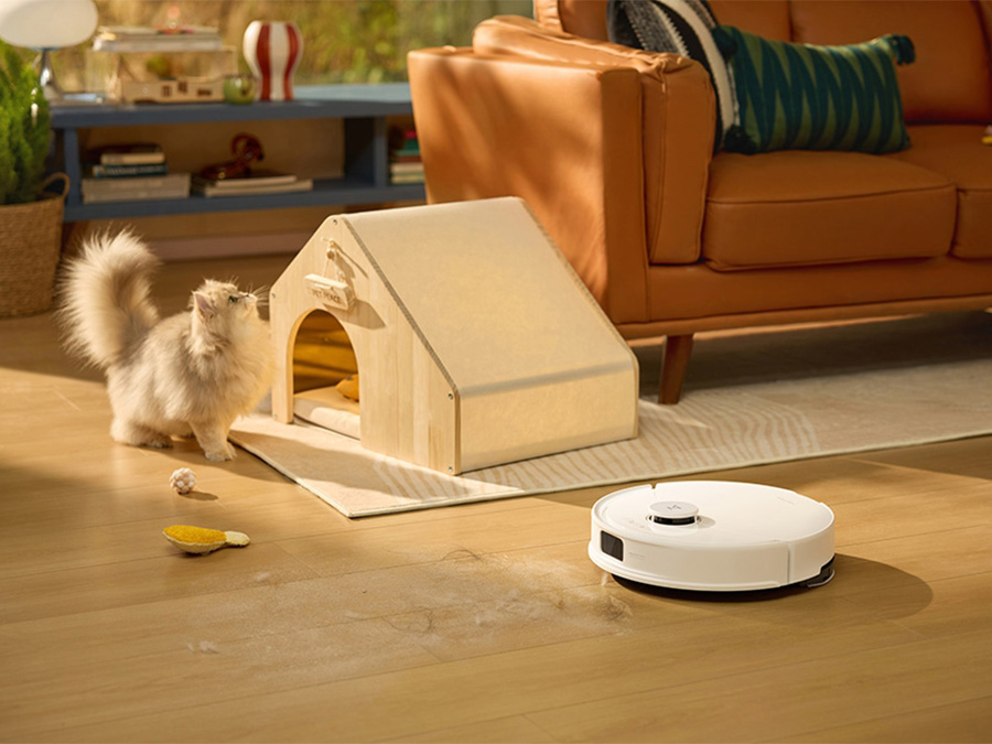 Der Staubsaugerroboter Roborock Q10 PF White saugt den Boden im Wohnzimmer; neben ihm eine weiße Katze und ein Tierhäuschen