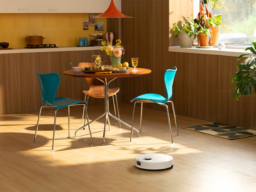 Der Staubsaugerroboter Roborock Q10 PF White saugt den Bereich neben einem Esstisch mit türkisfarbenen Stühlen