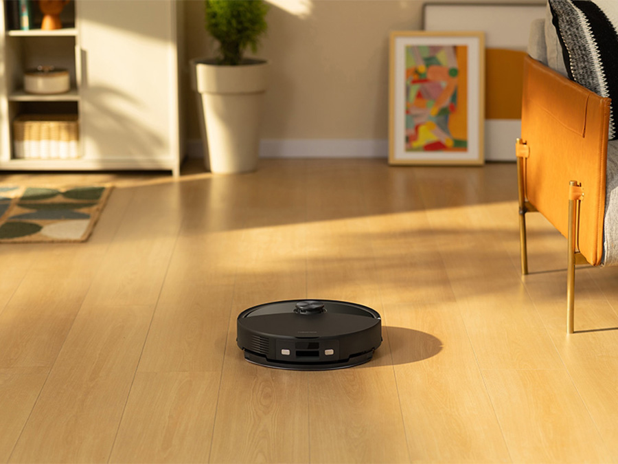Frau sitzt im Wohnzimmer und steuert den Staubsaugerroboter Roborock Q10 VF mit der App auf ihrem Smartphone