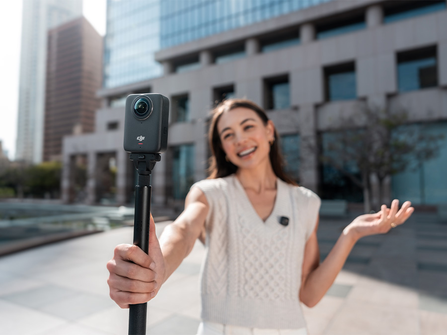Lächelnde Frau filmt mit DJI Osmo 360 Kamera auf Stativ in urbaner Umgebung