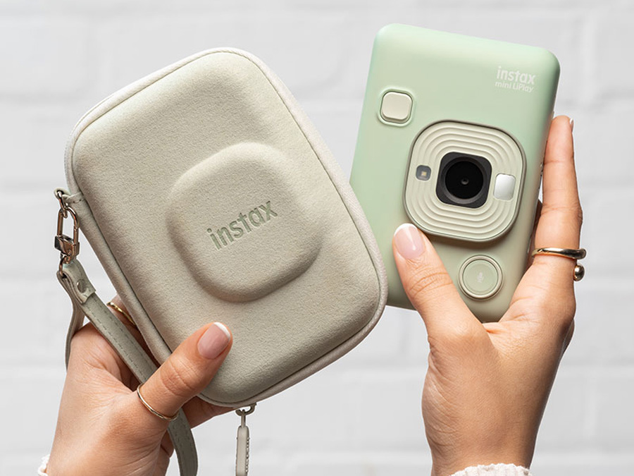 Grüne Fujifilm Instax Mini LiPlay Kamera neben Etui, gehalten in beiden Händen