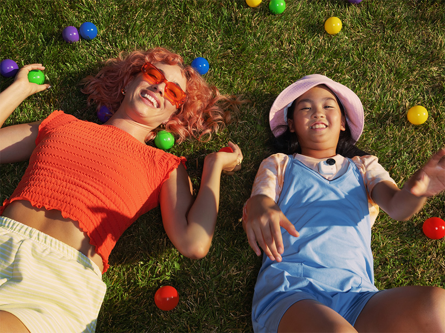 Zwei Personen liegen im Gras zwischen bunten Bällen, von oben aufgenommen mit der Insta360 GO Ultra in sommerlichen Farben