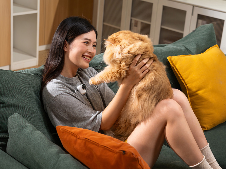 Frau sitzt auf dem Sofa mit einem Hund auf dem Schoß und trägt die Insta360 GO Ultra an der Bluse