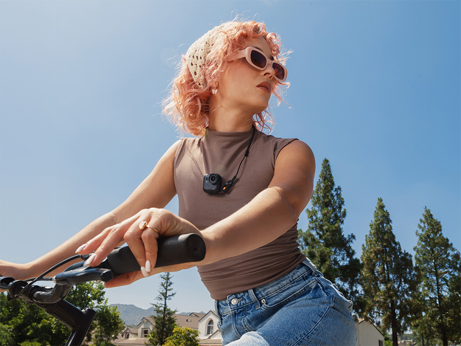 Frau fährt Fahrrad mit der Insta360 GO Ultra an einer Kordel auf der Brust; Aufnahmen während der Fahrt