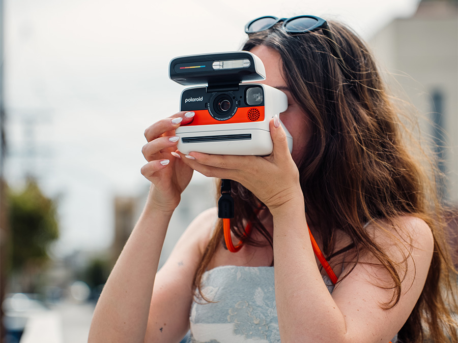 Frau macht ein Foto mit dem weißen Polaroid Flip Sofortbildkamera mit orangefarbenem Front und Tragegurt