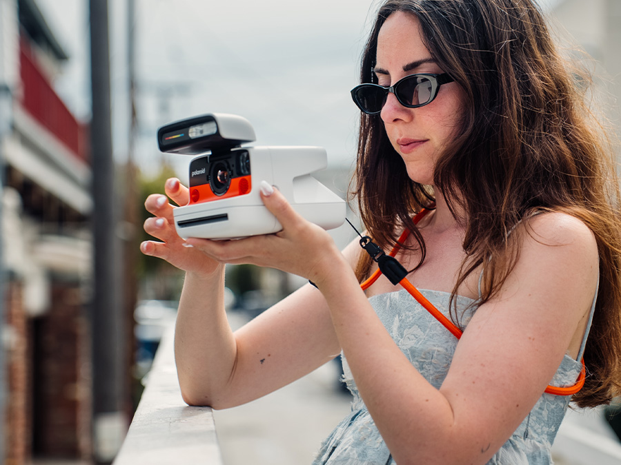 Frau hält mit beiden Händen die weiße Polaroid Flip Sofortbildkamera mit orangefarbenem Front, schaut auf das Gerät während der Bedienung